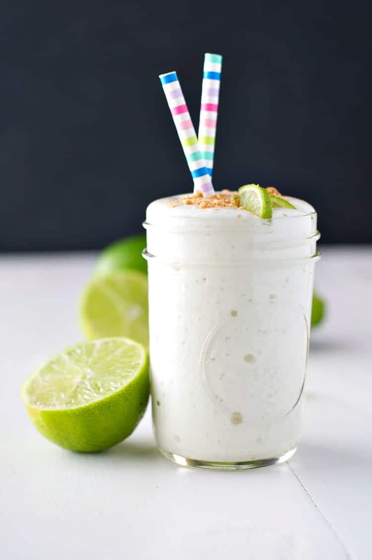 A glass jar filled with an easy key lime pie smoothie and two straws