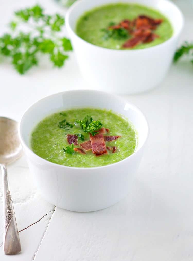 A close up of a small white bowl of sweet pea soup topped with bacon