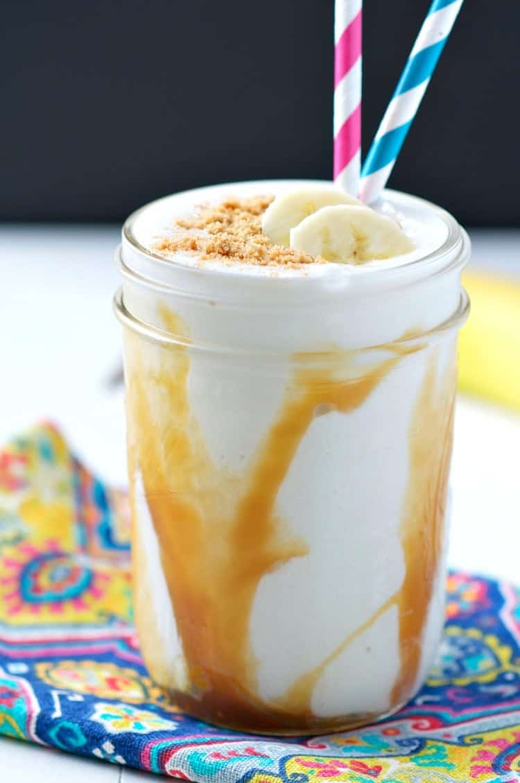 A mason jar filled with a banoffee pie smoothie, banana and two straws