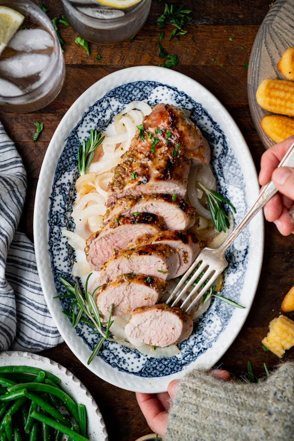 Fork on a platter of the best roast pork tenderloin recipe with rosemary and thyme.
