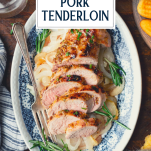 Close overhead image of a blue and white platter with roasted pork tenderloin and text title overlay