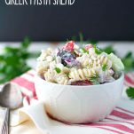 A Greek pasta salad in a bowl with a spoon at the side