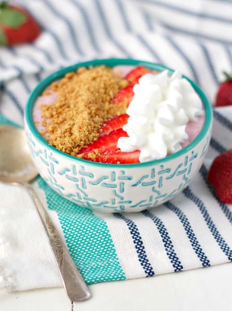 A close up of a strawberry cheesecake smoothie bowl with a spoon and topped with cream
