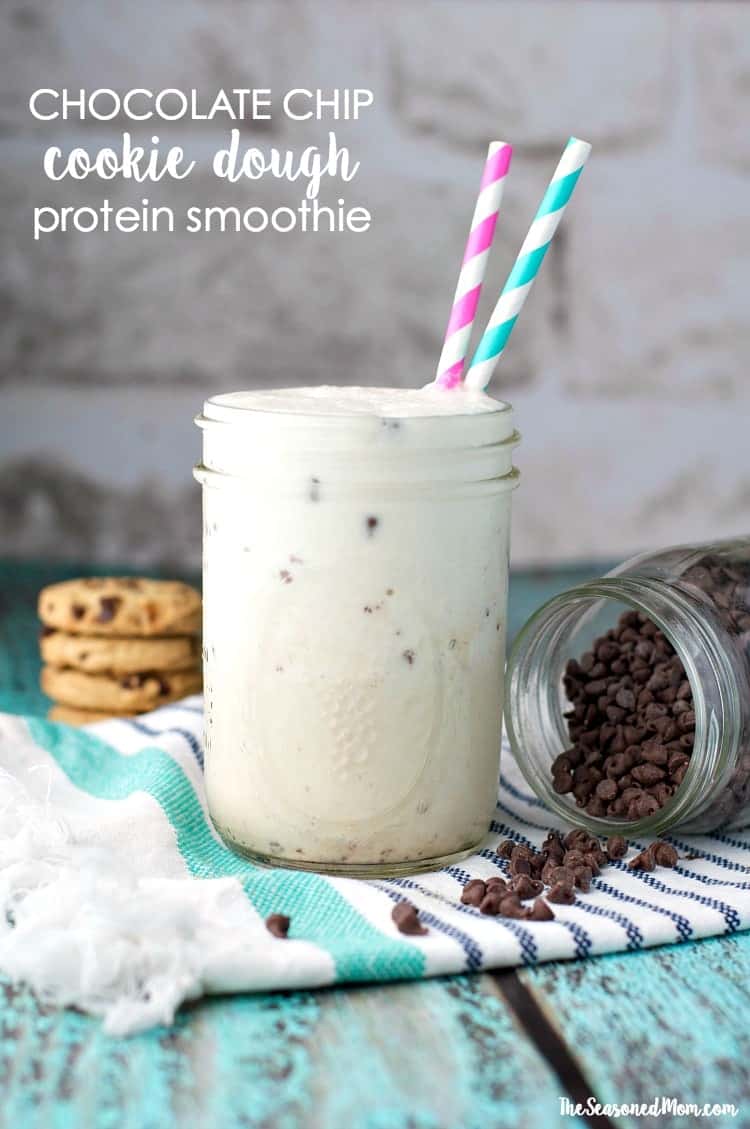 A mason jar filled with a cookie dough smoothie with two straws and chocolate chips beside it