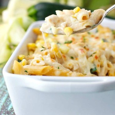 A close up of a chicken pasta casserole with a serving spoon lifting up a spoonful