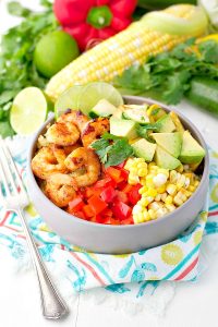 Bowl of marinated shrimp and summer vegetables in a bowl with quinoa and diced avocado