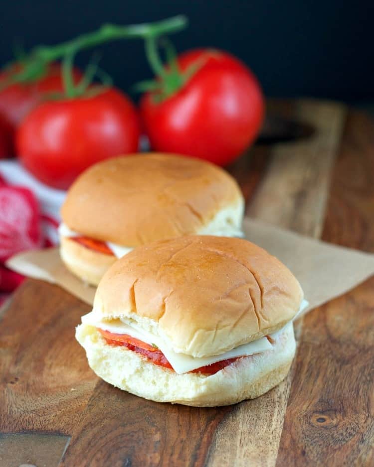 A picnic sandwich with cheese and tomatoes in the background