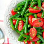 Close overhead shot of green bean salad with tomatoes in a white bowl