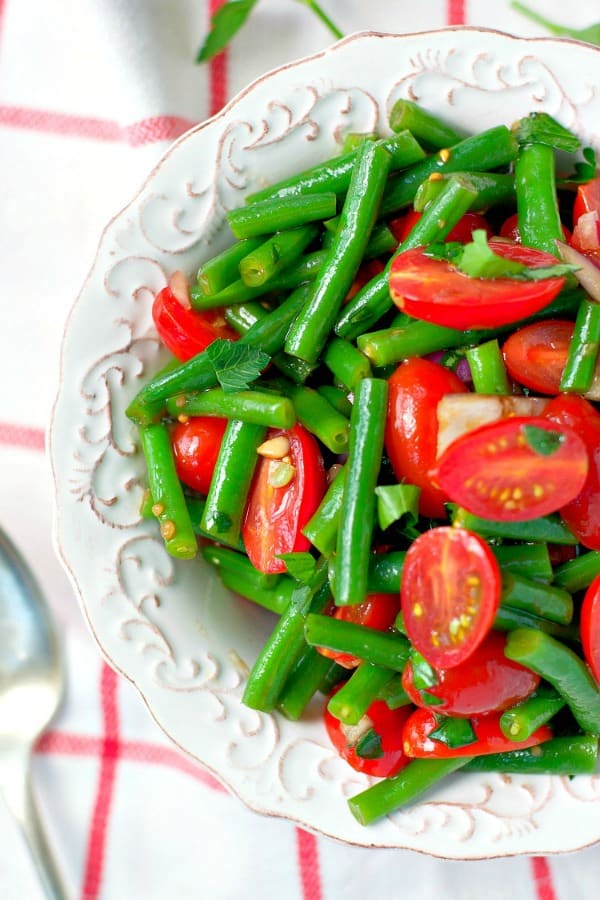 Close overhead shot of green bean salad with tomatoes in a white bowl