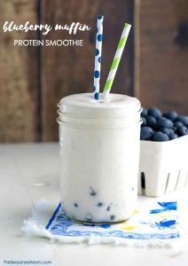 A blueberry muffin protein smoothie in a glass with two straws
