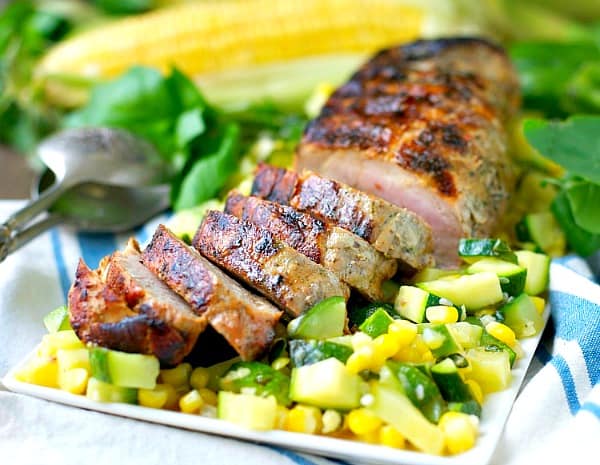Horitzontal shot of a grilled pork tenderloin on a serving plate over corn and zucchini
