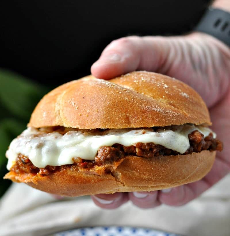 A hand holding a sloppy joe with melted cheese on top