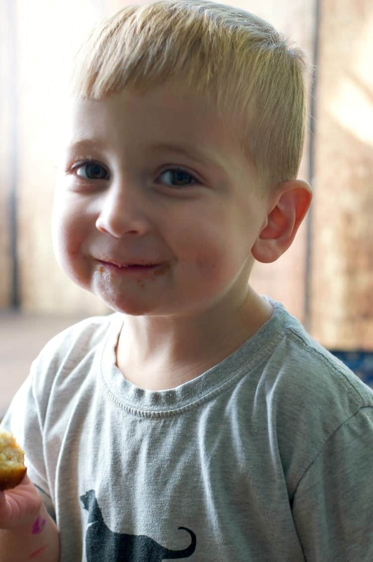 A little boy eating cinnamon sugar puff muffins with one in his hand