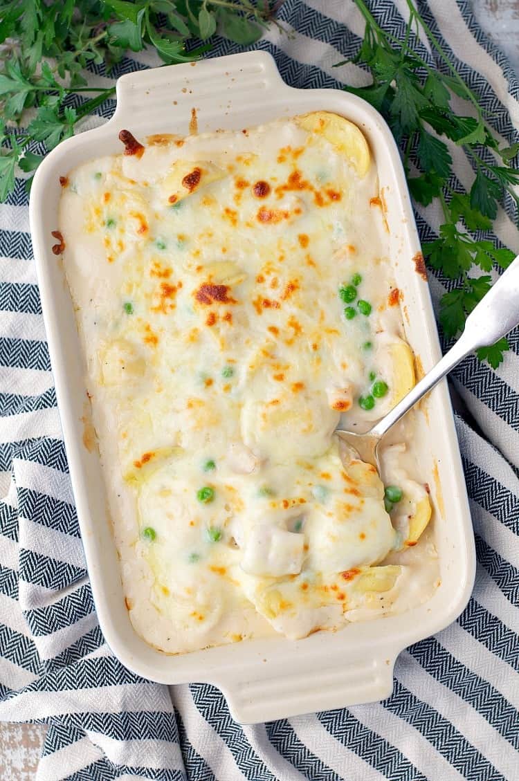 An overhead shot of Chicken & Ravioli in Alfredo Sauce in a casserole dish with a serving spoon