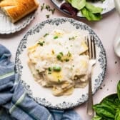 Horizontal overhead shot of chicken ravioli alfredo on a blue and white plate with a side salad and bread.