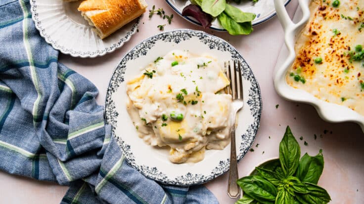 Horizontal overhead shot of chicken ravioli alfredo on a blue and white plate with a side salad and bread.