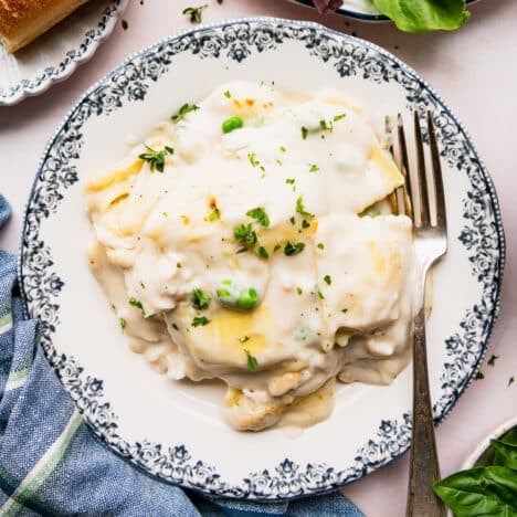 Square overhead shot of chicken ravioli alfredo on a blue and white plate with a side salad and bread.