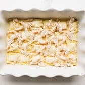 Adding a layer of chicken on top of the ravioli.