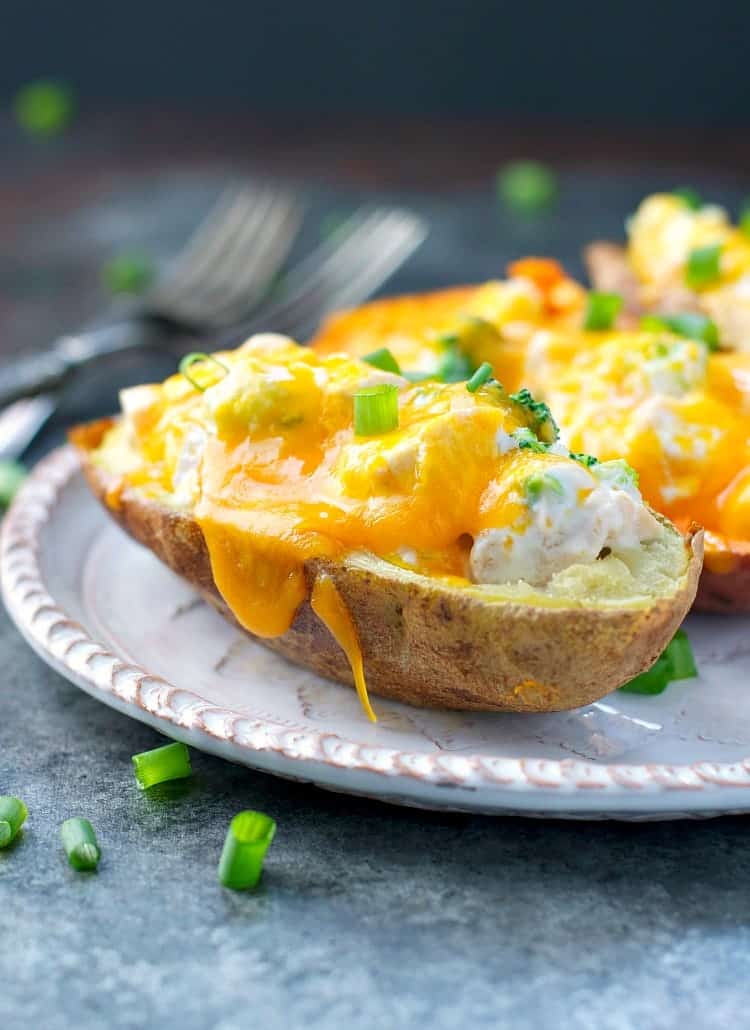 A close up of cheese stuffed potatoes on a plate topped with green onion