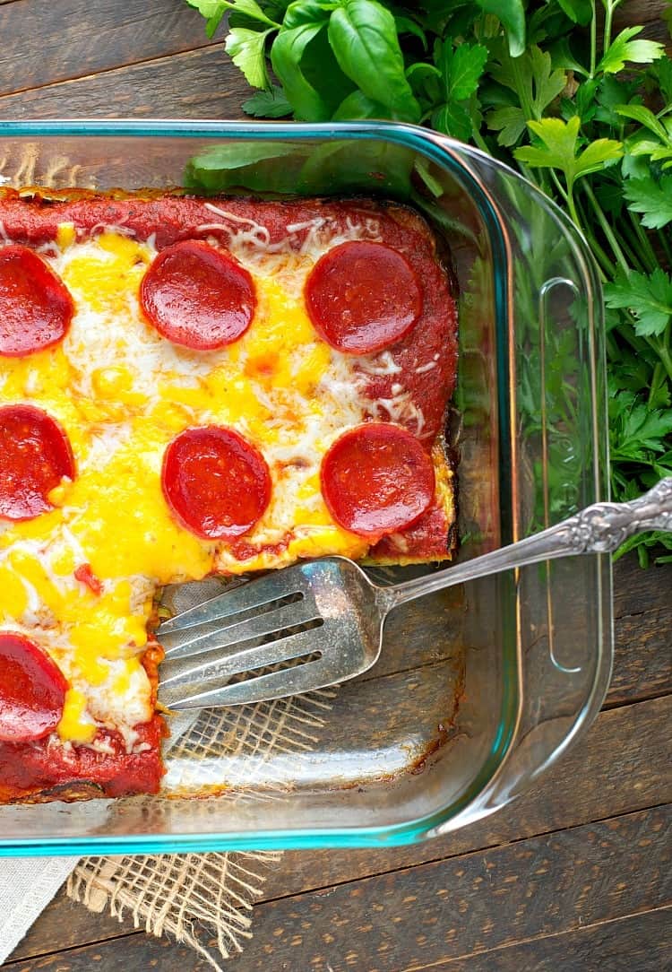 A zucchini pizza casserole in a glass dish with a spatula