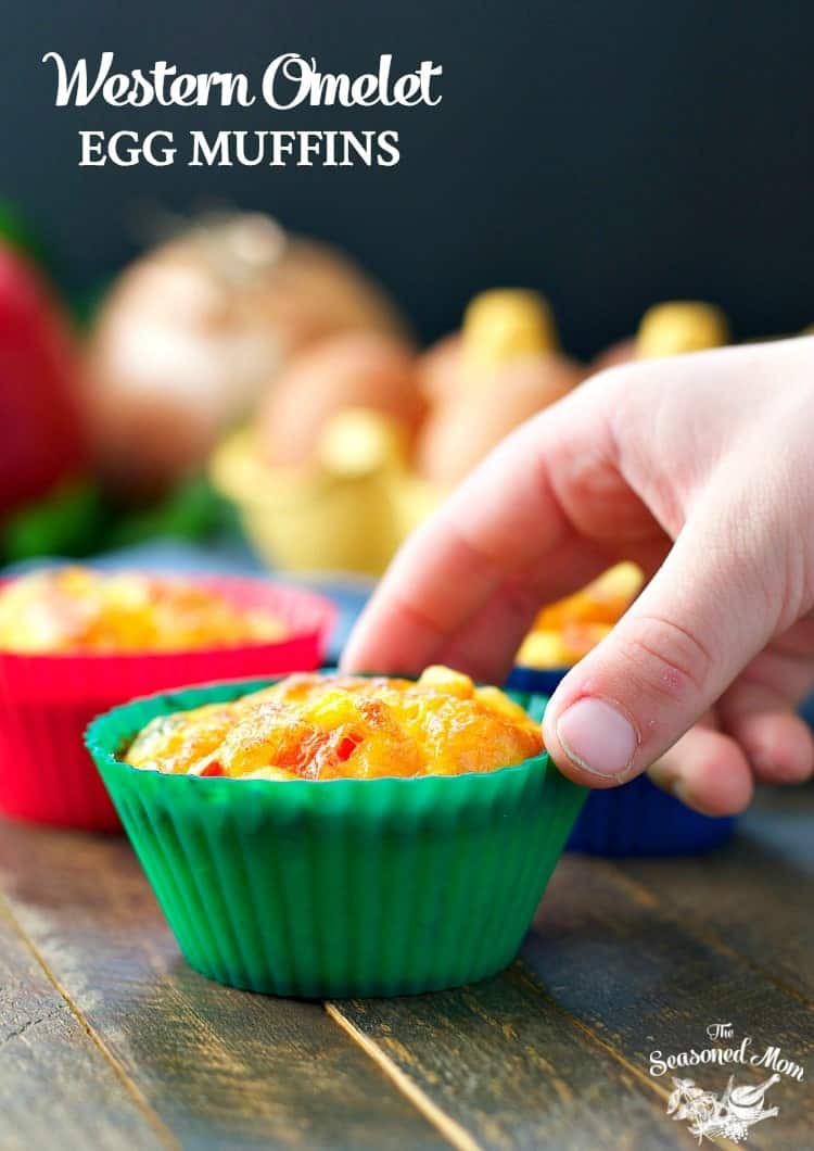 A person's hand grabs a small egg omelet muffin bite in a green silicone muffin cup.