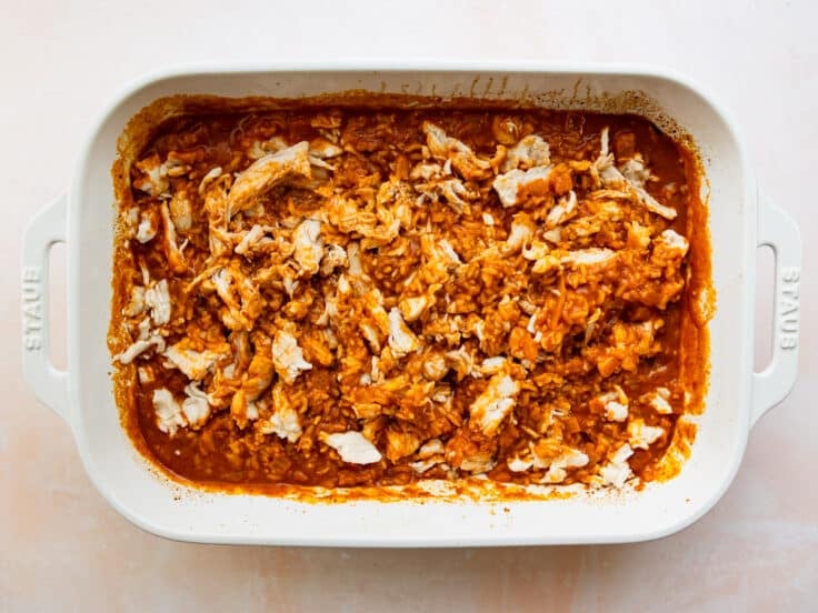 Adding rotisserie chicken to the partially cooked casserole.