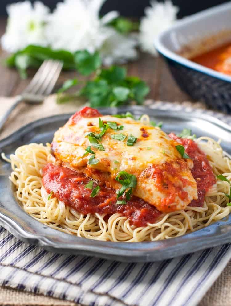 Healthy baked chicken parmesan on a plate of spaghetti with fresh basil