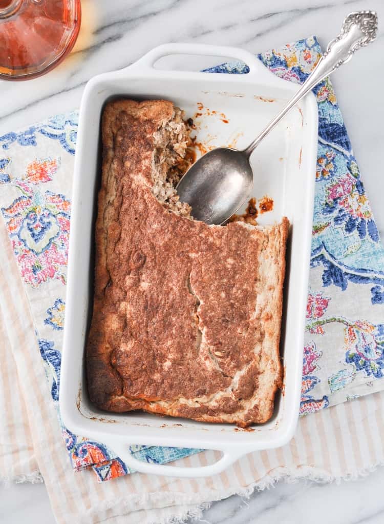 An overhead shot of a healthy baked oatmeal in a white baking dish with a large serving spoon