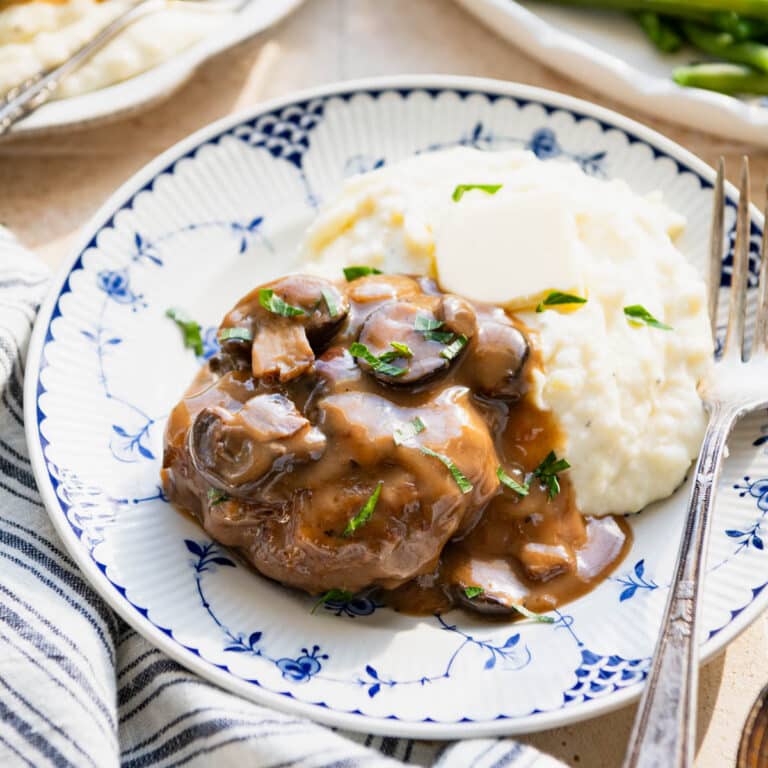 Square side shot of slow cooker salisbury steak on a plate with mashed potatoes.
