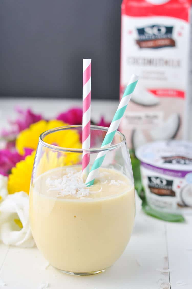 A side shot of a coconut smoothie in a glass with two straws 