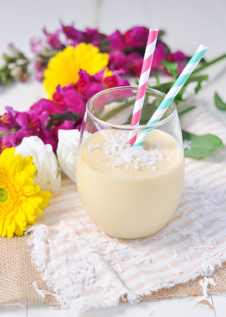 A photo of a coconut smoothie in a glass with straws and topped with coconut