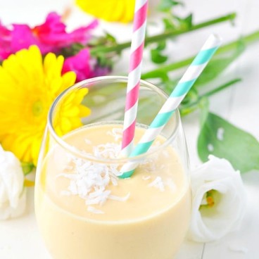 Overhead shot of a tropical coconut smoothie in a glass surrounded by flowers