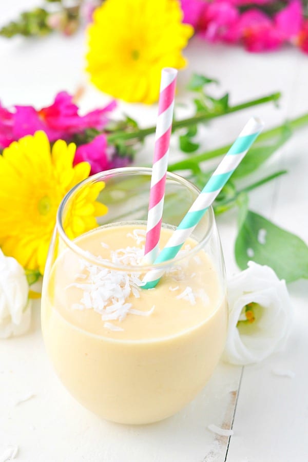 Overhead shot of a tropical coconut smoothie in a glass surrounded by flowers
