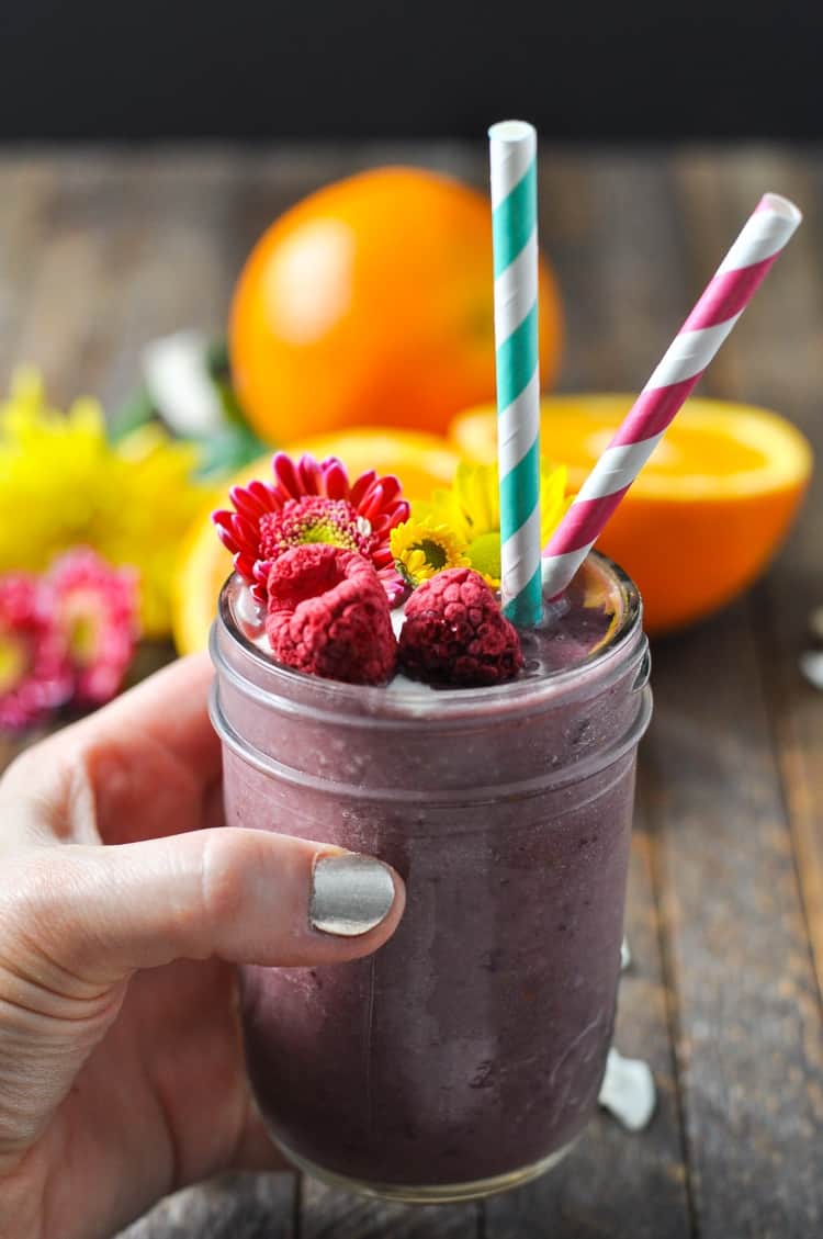 A hand holding a southern ambrosia smoothie with two straws and dried fruit on top