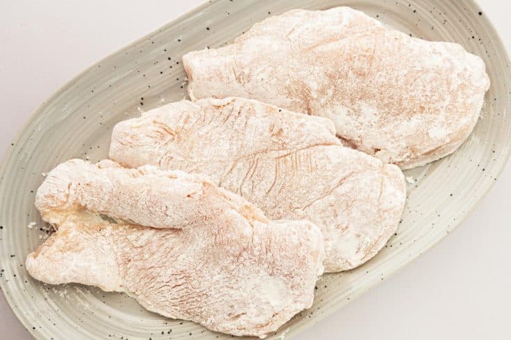 Dredging chicken cutlets in seasoned flour.