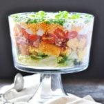 Layered Southern Cornbread Salad with bacon and cheese in a large glass serving bowl