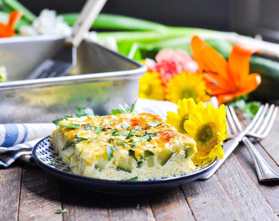 A close up of a baked zucchini and parmesan omelet on a plate with flowers in the background, easy zucchini recipes