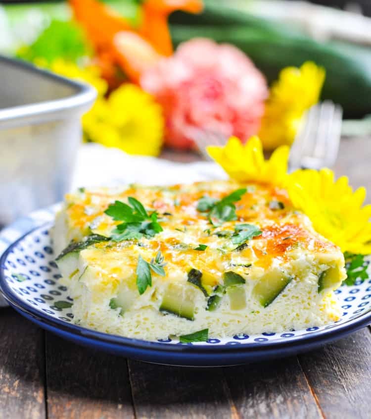A close up of a baked zucchini and parmesan omelet on a plate with flowers in the background, easy zucchini recipes