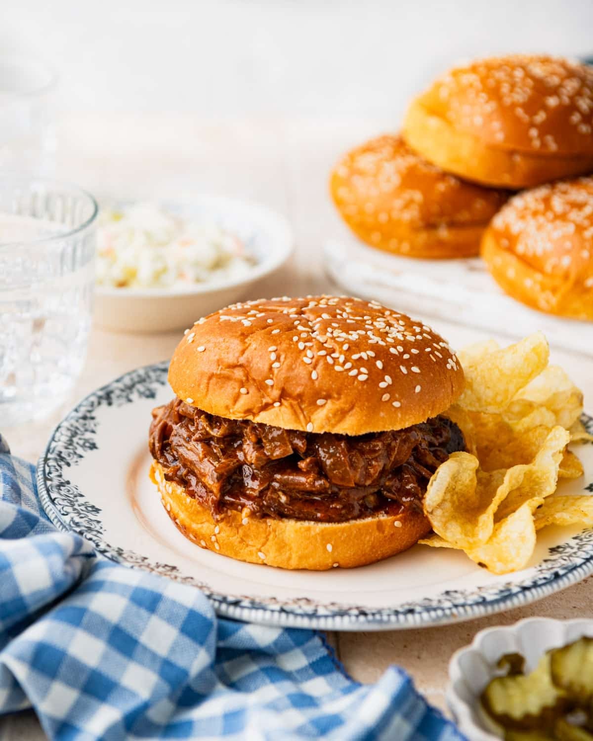 Bbq beef sandwich on a plate with a side of chips and coleslaw.