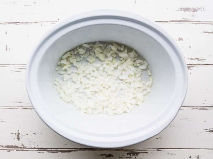 Diced onion in the bottom of a slow cooker.