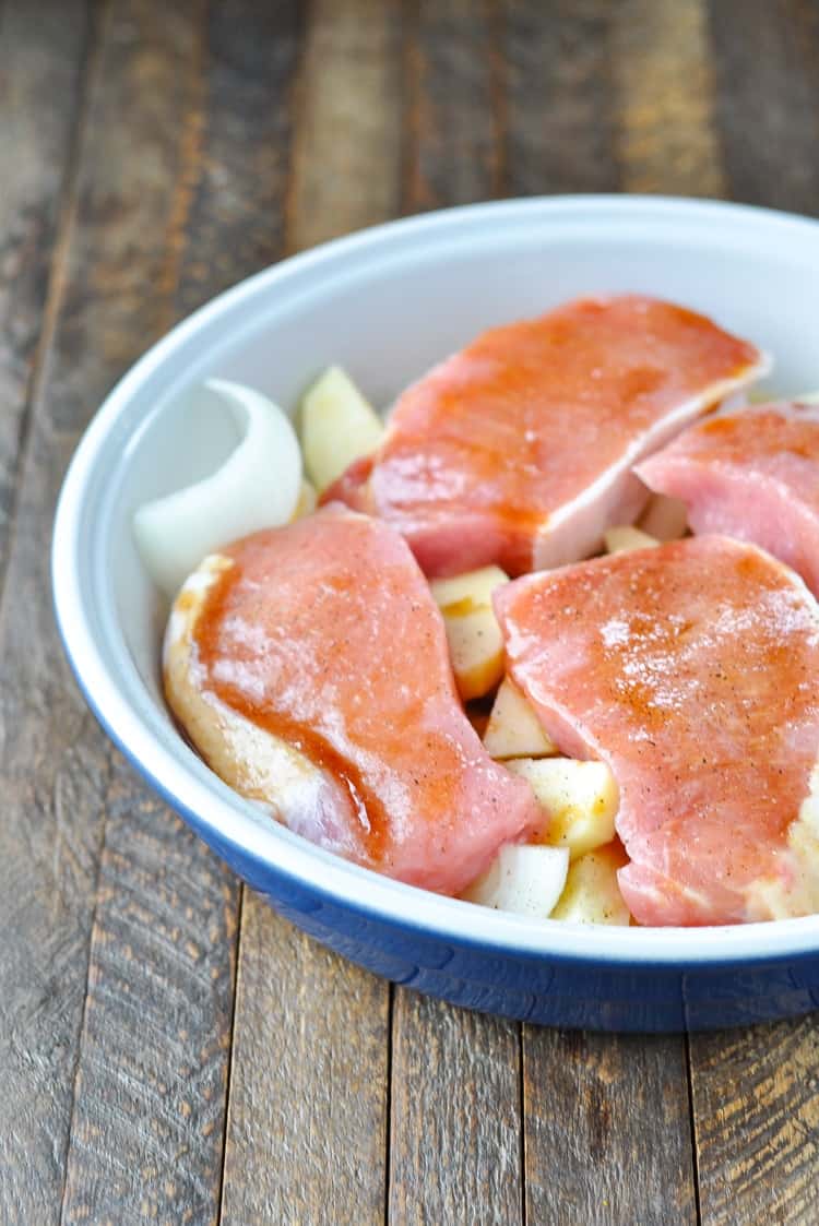 Boneless pork chops in a baking dish on top of apple before being cooked