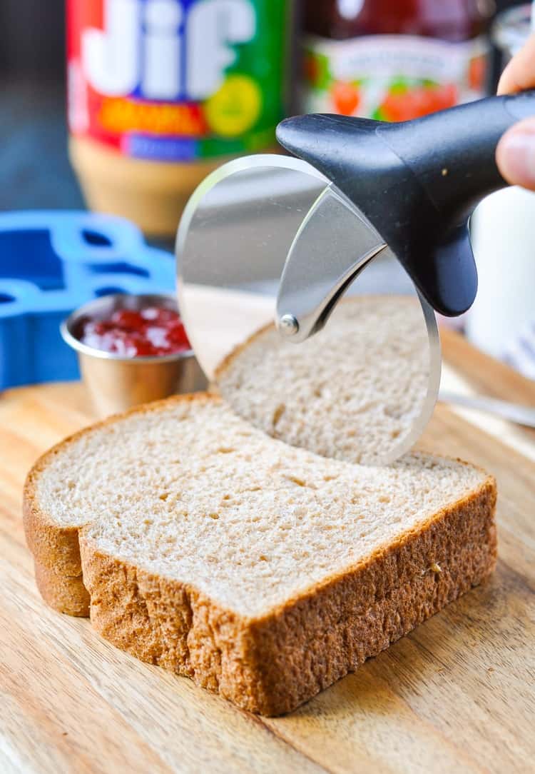 A close up of cutting the crusts of a peanut butter and jelly sandwich