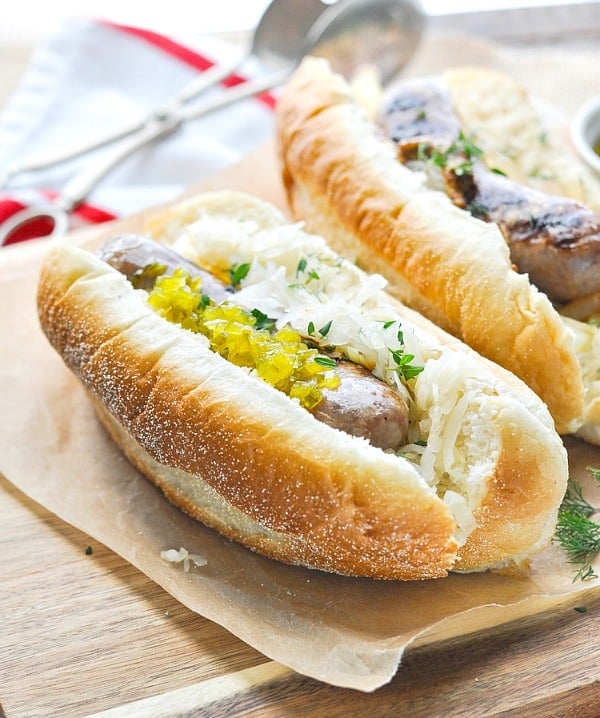 Grilled beer brats in hoagie rolls on a cutting board