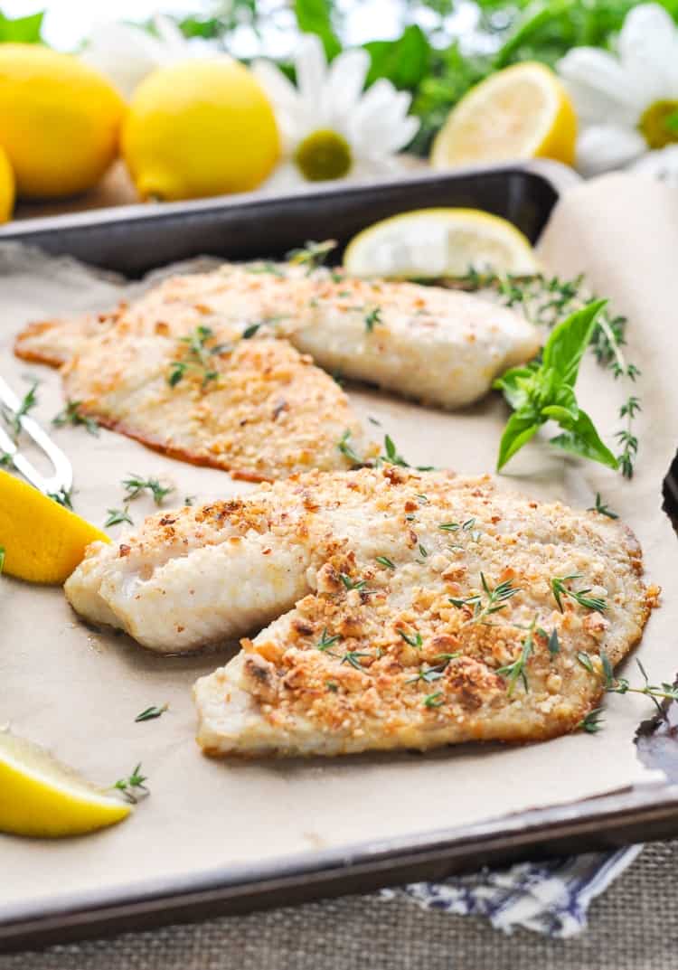 Almond encrusted Tilapia on a baking sheet with lemon wedges
