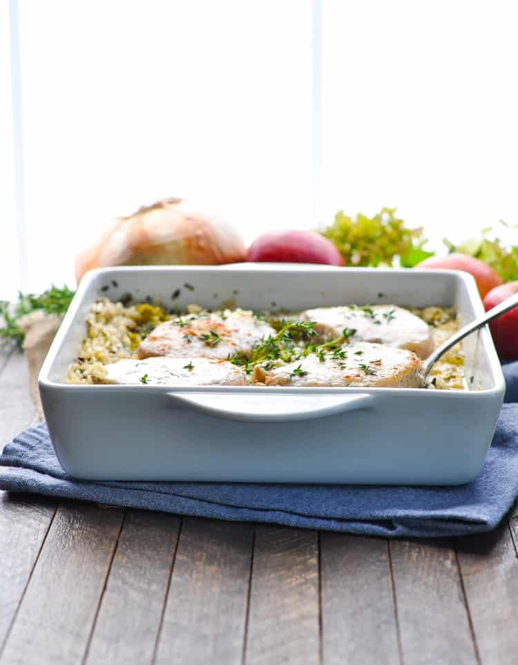A pork chop casserole in a white dish topped with fresh herbs