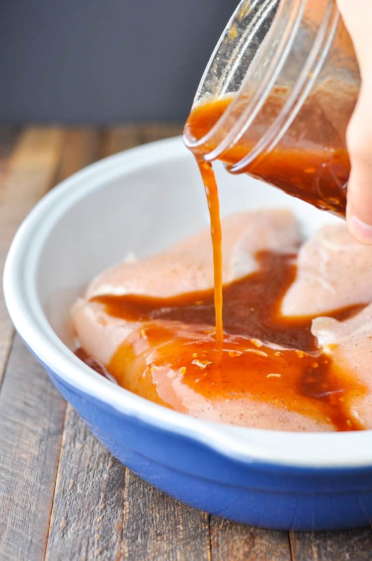 Pouring sauce over Honey French Baked Chicken Breasts in a casserole dish