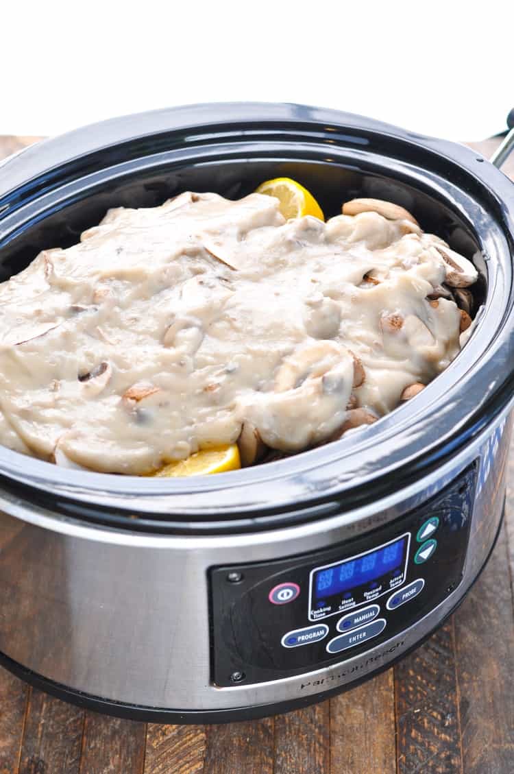 Mushroom gravy in a slow cooker on top of mushrooms and pork chops