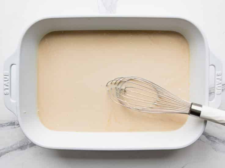 Whisking together the creamy sauce for a beef stroganoff casserole in a white dish.