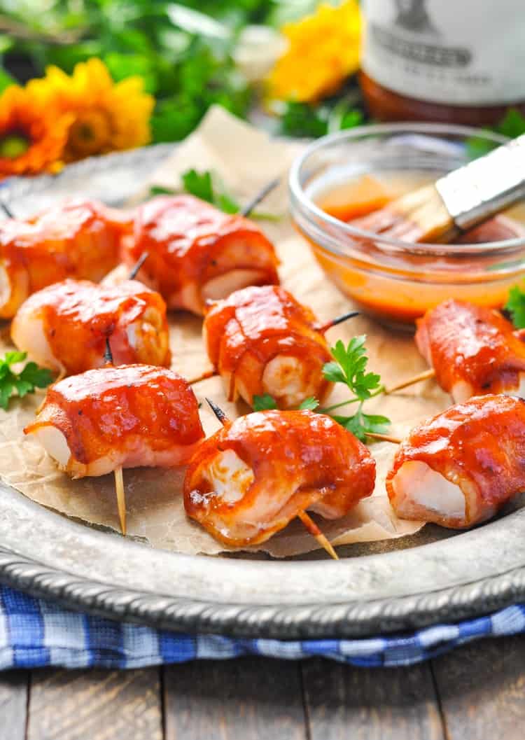 A close up of bacon wrapped chicken bites on cocktail sticks sitting on a serving plate