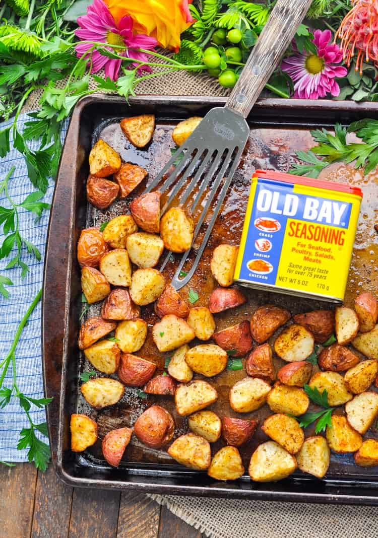 Crispy seasoned red potatoes on a sheet pan with old bay seasoning and a spatula at the side